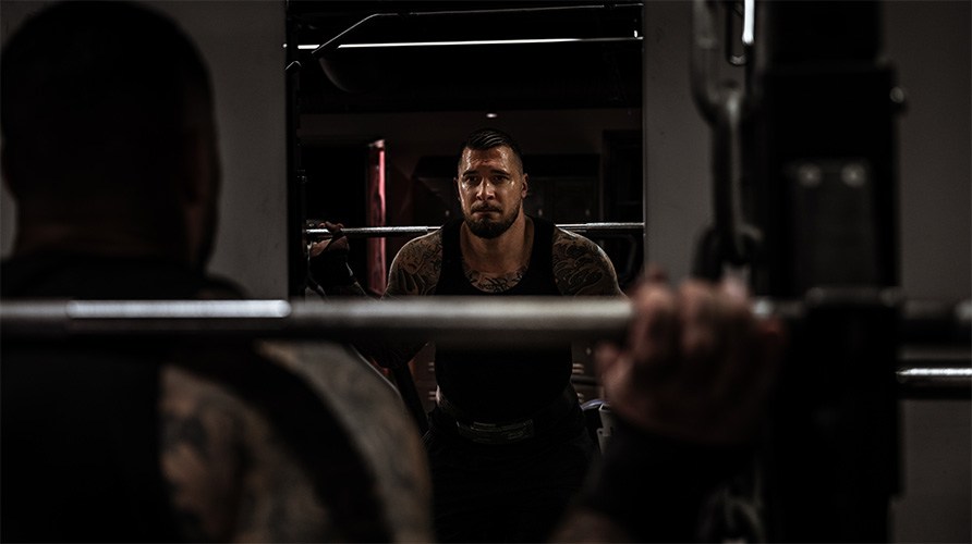 En man i tr�ningsmilj� framf�r en spegel f�r sig redo at g�ra en kn�b�j med st�ng. 