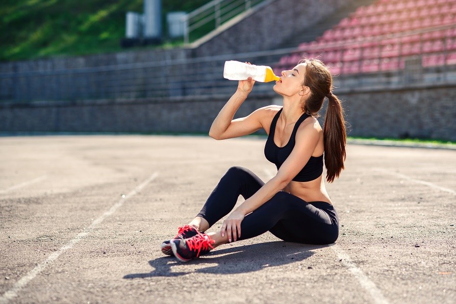Träningsklädd kvinna som sitter ner på löparbana och dricker.