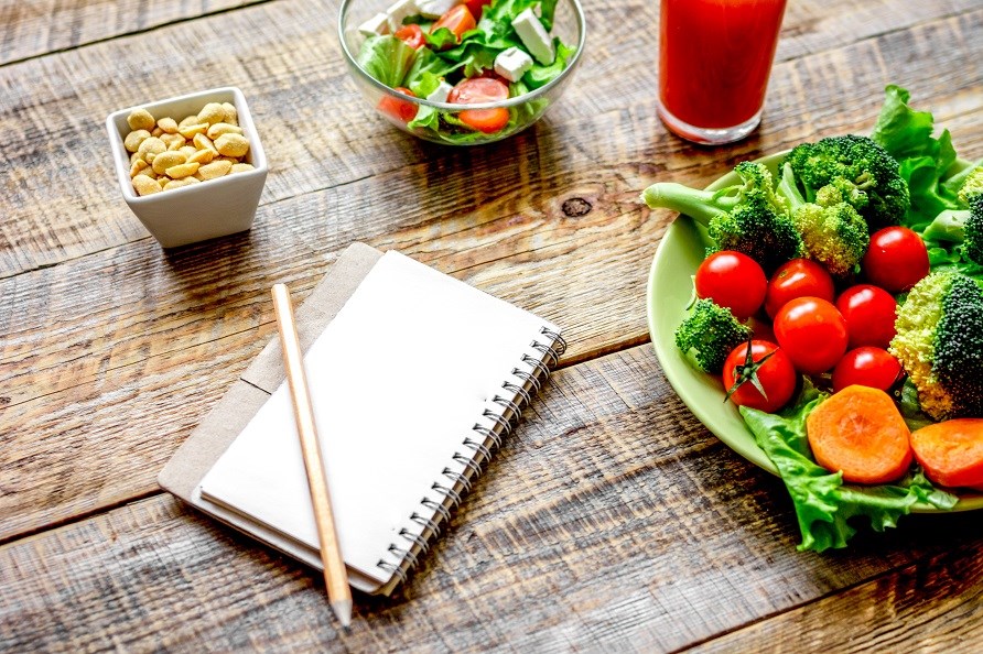 Bild på ett bord med ett anteckningsblock, skål med nötter och två skålar men grönsaker. 