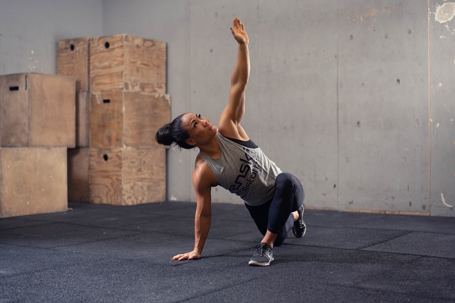 Kvinna som kör dynamisk stretch inne på ett gym.