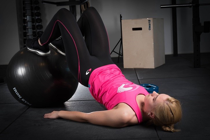 Tjej som gör lårcurl med pilatesboll på gym. Tjej som gör lårcurl med pilatesboll på gym.