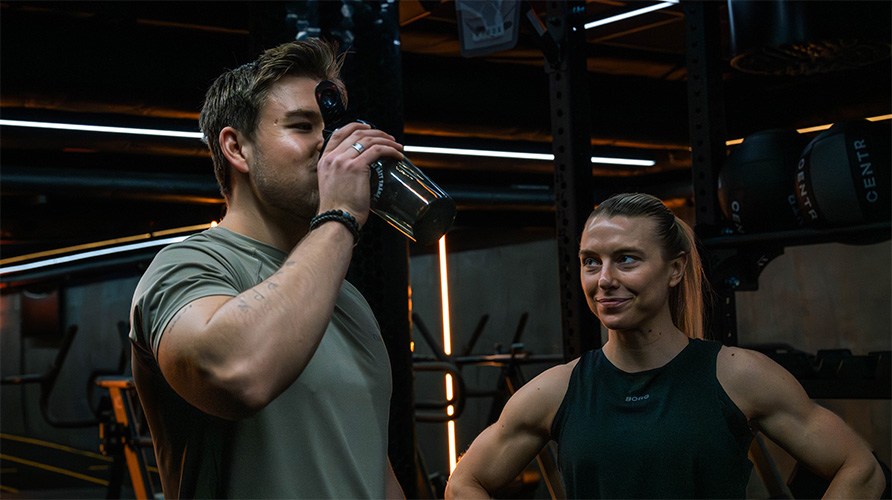 Kvinna och man i gymmilj�, mannen dricker en proteinshake.