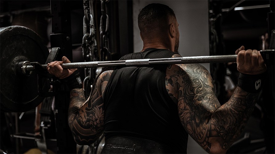 En man med muskul�s rygg st�r vid en skivst�ng.