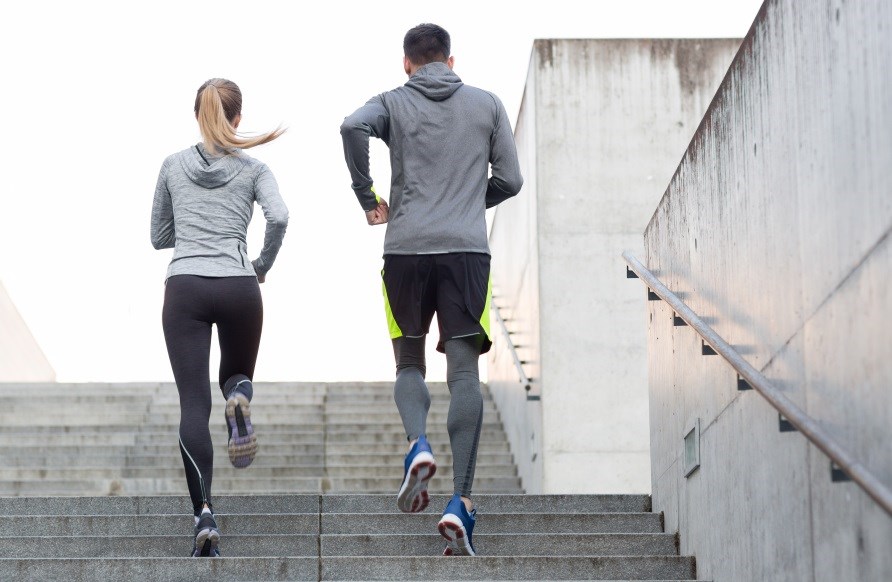 En kvinna och en man iklädda träningskläder som springer upp för en trappa.